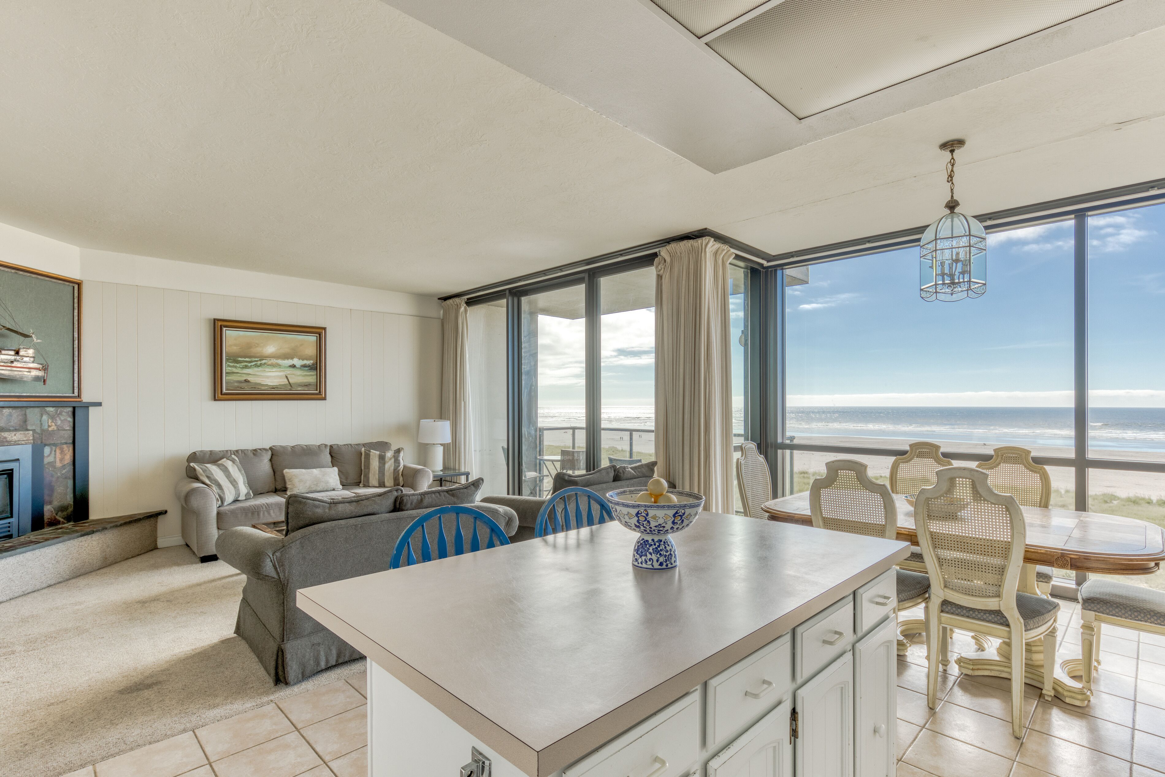 A spacious living area with a large window overlooking the beach, a dining table with chairs, and a cozy seating arrangement.