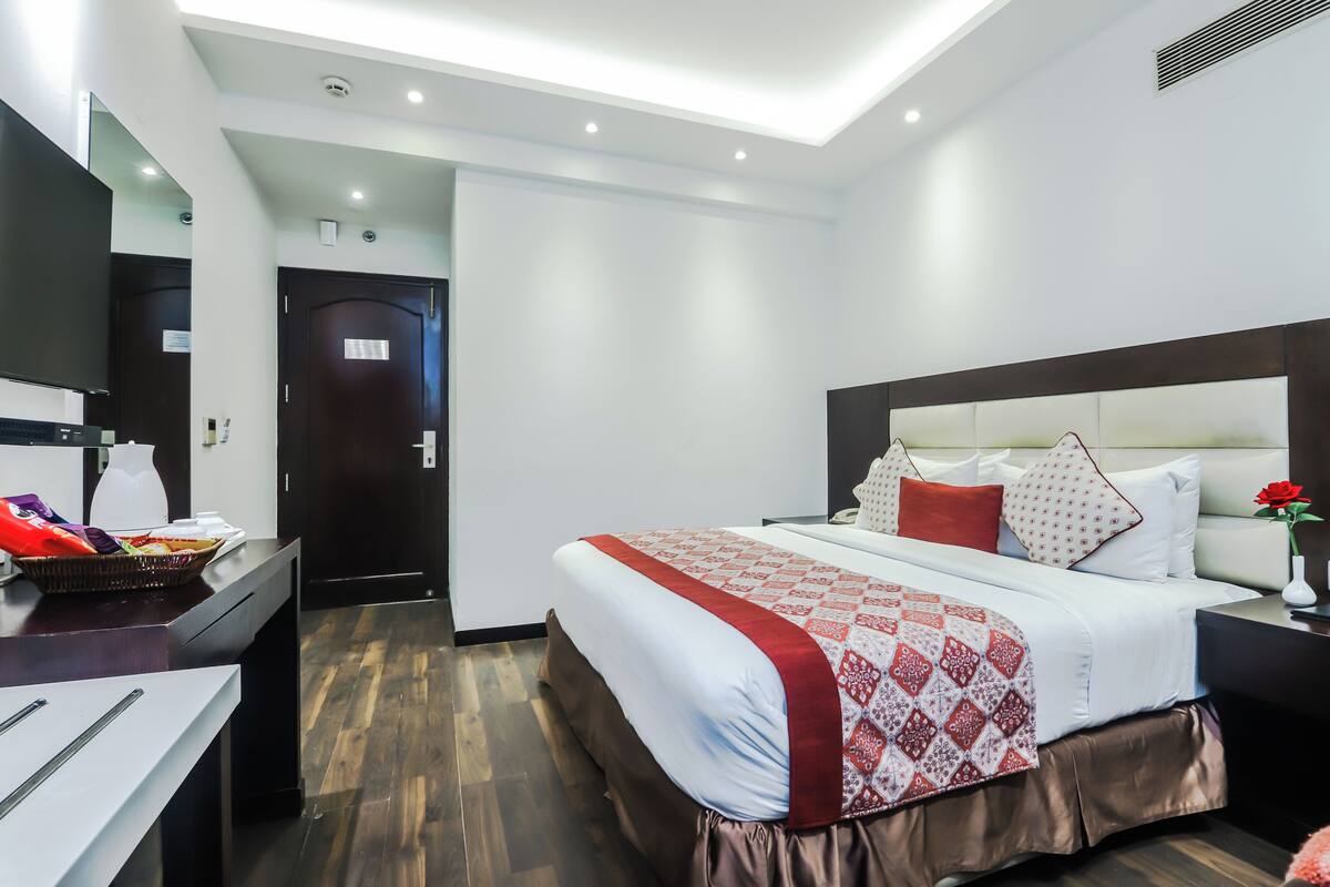 Una habitación de hotel con cama, mesita de noche y escritorio con una cesta de aperitivos.