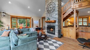 A spacious living room with a large sectional sofa, a fireplace, and a kitchen area visible through an open door. - Après Chalet|Ski|Luxury|Sauna|HotTub|Firepit|Disco (Windham)