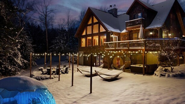 A log cabin with a balcony, outdoor seating, and a snow-covered ground. - Après Chalet|Ski|Luxury|Sauna|HotTub|Firepit|Disco (Windham)