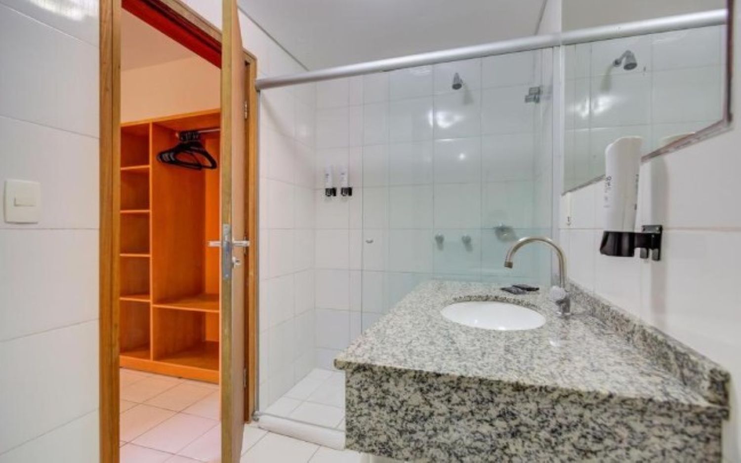 A bathroom with a granite countertop sink, a glass shower enclosure, and a wooden closet with hanging space.
