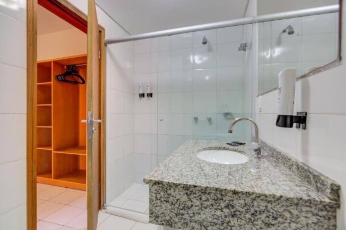 Un baño con lavamanos de encimera de granito, cabina de ducha de vidrio y armario de madera con espacio para colgar.