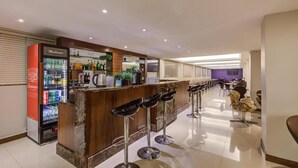 Zona de bar con mostrador, taburetes y un refrigerador lleno de bebidas.