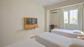 Een hotelkamer met twee eenpersoonsbedden, een televisie bevestigd aan een houten plank, een airconditioning en een raam met gordijnen.