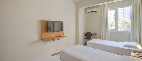 A hotel room with two single beds, a TV mounted on a wooden shelf, an air conditioning unit, and a window with curtains.