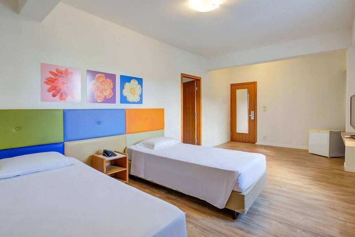 Una habitación de hotel con dos camas, piso de madera, un escritorio con silla, televisión y una puerta.