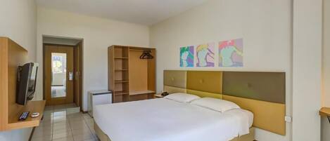 Una habitación de hotel con una cama grande, un armario, un televisor y un escritorio pequeño.