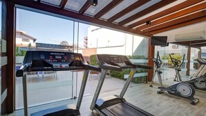 Un gimnasio con cintas de correr, bicicletas estáticas y un amplio ventanal con vistas al exterior.