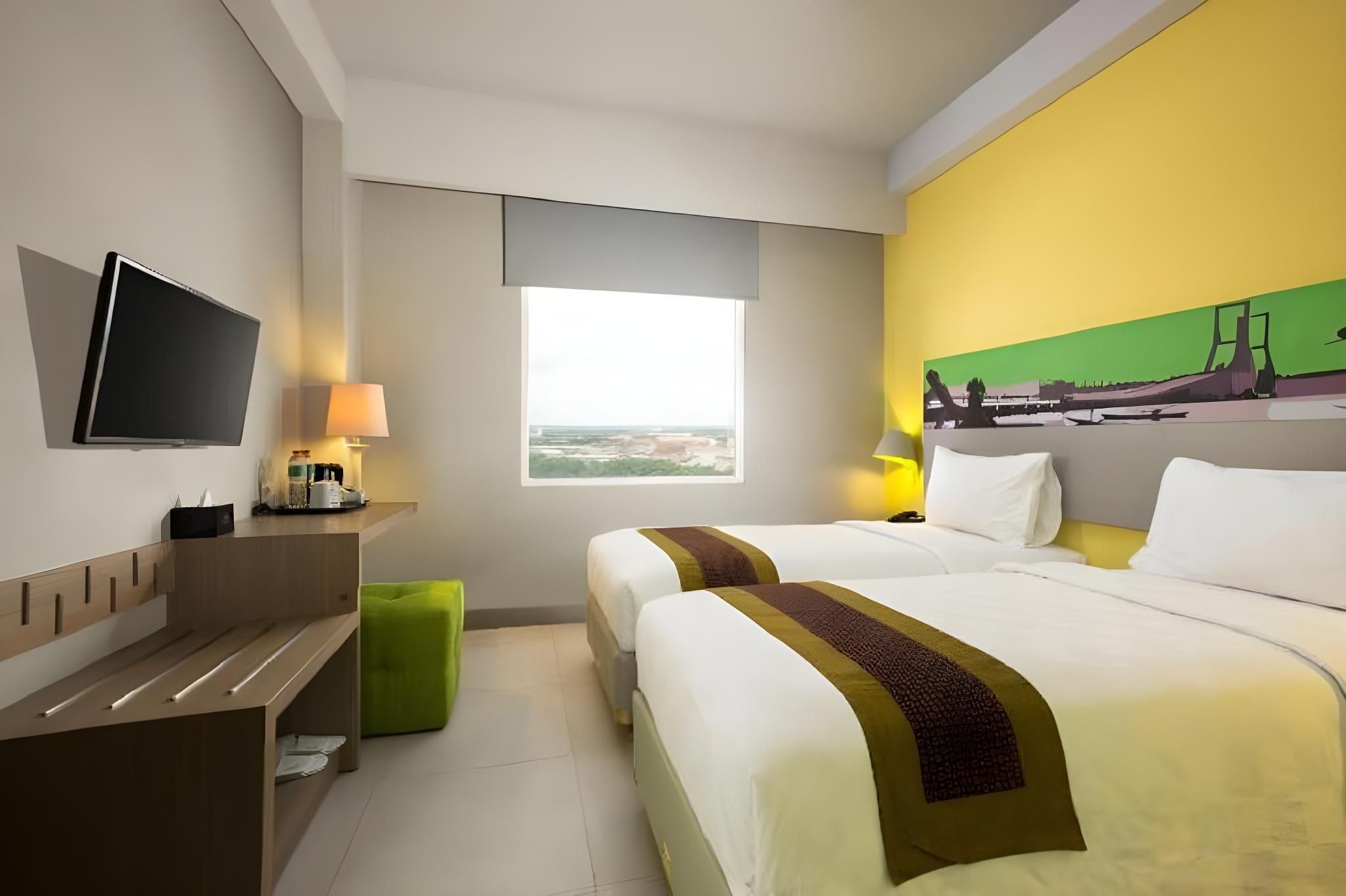 Een hotelkamer met twee bedden, een televisie, een bureau, een lamp en een schilderij aan de muur.