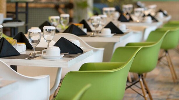 A restaurant with white tables and green chairs, each set with a white plate, a glass, and a napkin. - Khas Surabaya Hotel (Pabean Cantikan)
