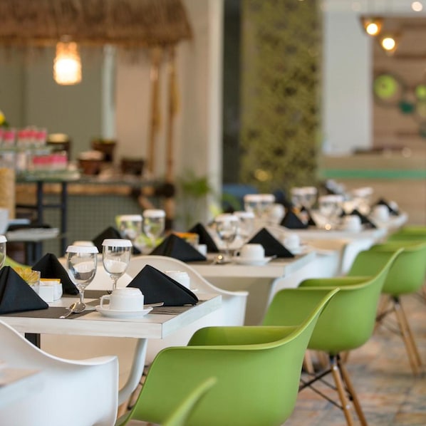 A restaurant with white tables and green chairs, each set with a white plate, a glass, and a napkin.