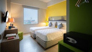 A hotel room with two beds, a desk with a lamp, a green cabinet, and a view of a cityscape through a window. - Khas Surabaya Hotel (Pabean Cantikan)