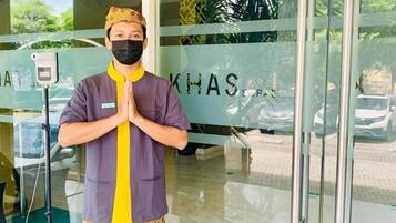 A person standing in front of a building entrance with a glass door, wearing a traditional outfit with a yellow and purple shirt, a patterned apron, and a headpiece.