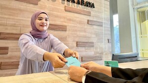 A person handing over a card to another person at a reception desk with a wooden wall and a sign that reads "KHAS SURABAYA". - Khas Surabaya Hotel (Pabean Cantikan)