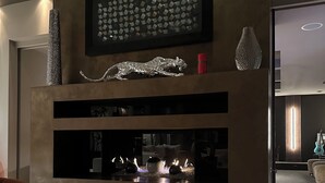 Una sala de estar moderna con chimenea, una obra de arte abstracta enmarcada y una escultura metálica decorativa.
