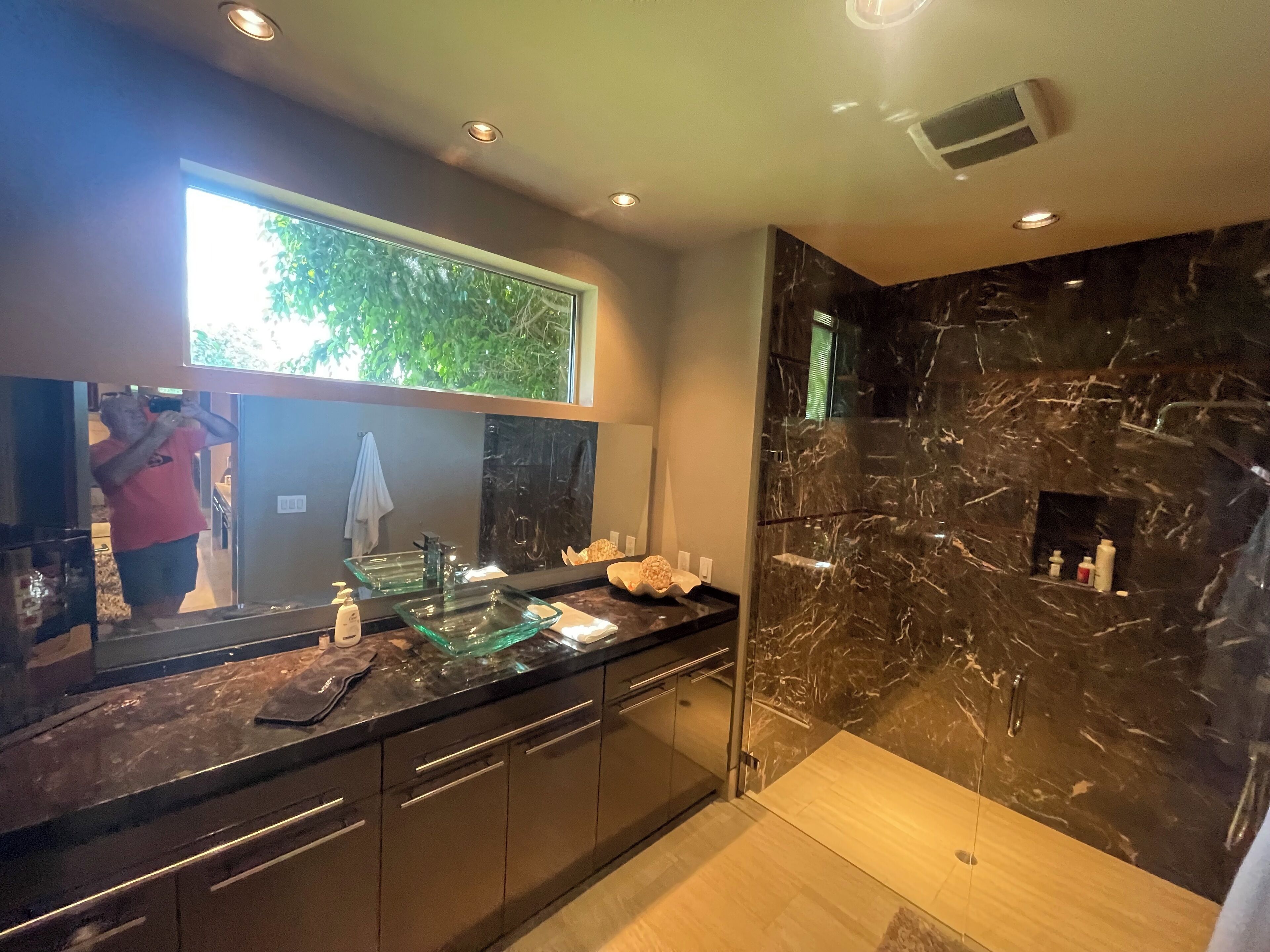 Un baño moderno con un lavabo de vidrio, paredes de mármol oscuro y un espejo grande.
