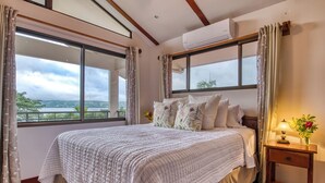 A bedroom with a large bed, a nightstand, a lamp, and a view of the outdoors. - Bonita Apt. Amazing 2nd floor Apt - Views Galore! (Tilarán)
