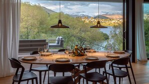A dining area with a large round table set for six, overlooking a scenic mountainous landscape. - Willow Waters | Lakeside luxury with all day sunshine & fantastic outdoor living (Kawarau Falls)