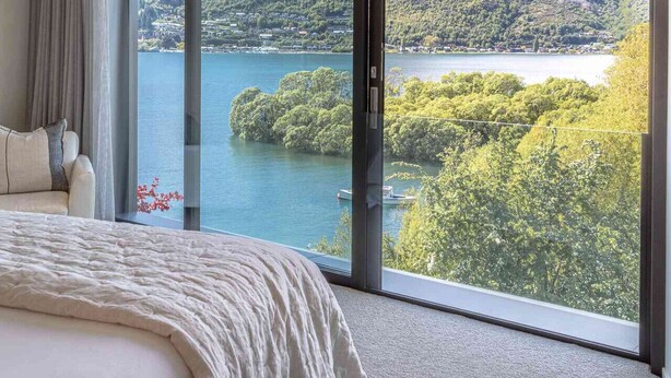 A bedroom with a large window offering a view of a lake and mountains. - Willow Waters | Lakeside luxury with all day sunshine & fantastic outdoor living (Kawarau Falls)