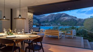 A dining area with a table set for four, overlooking a mountainous landscape and a body of water. - Willow Waters | Lakeside luxury with all day sunshine & fantastic outdoor living (Kawarau Falls)