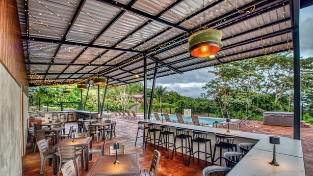 An outdoor dining area with tables and chairs, a pool, and a covered patio with string lights.
