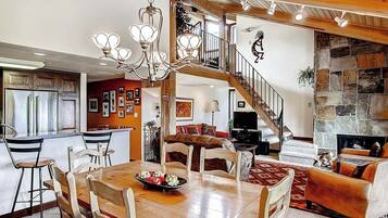 A spacious living area with a wooden dining table, a staircase leading to an upper level, and a stone fireplace.