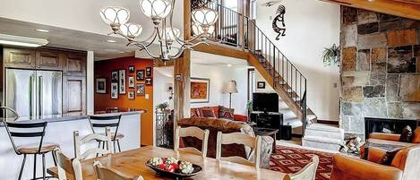 Amplia sala de estar con una mesa de comedor de madera, una escalera que lleva a un nivel superior y una chimenea de piedra.