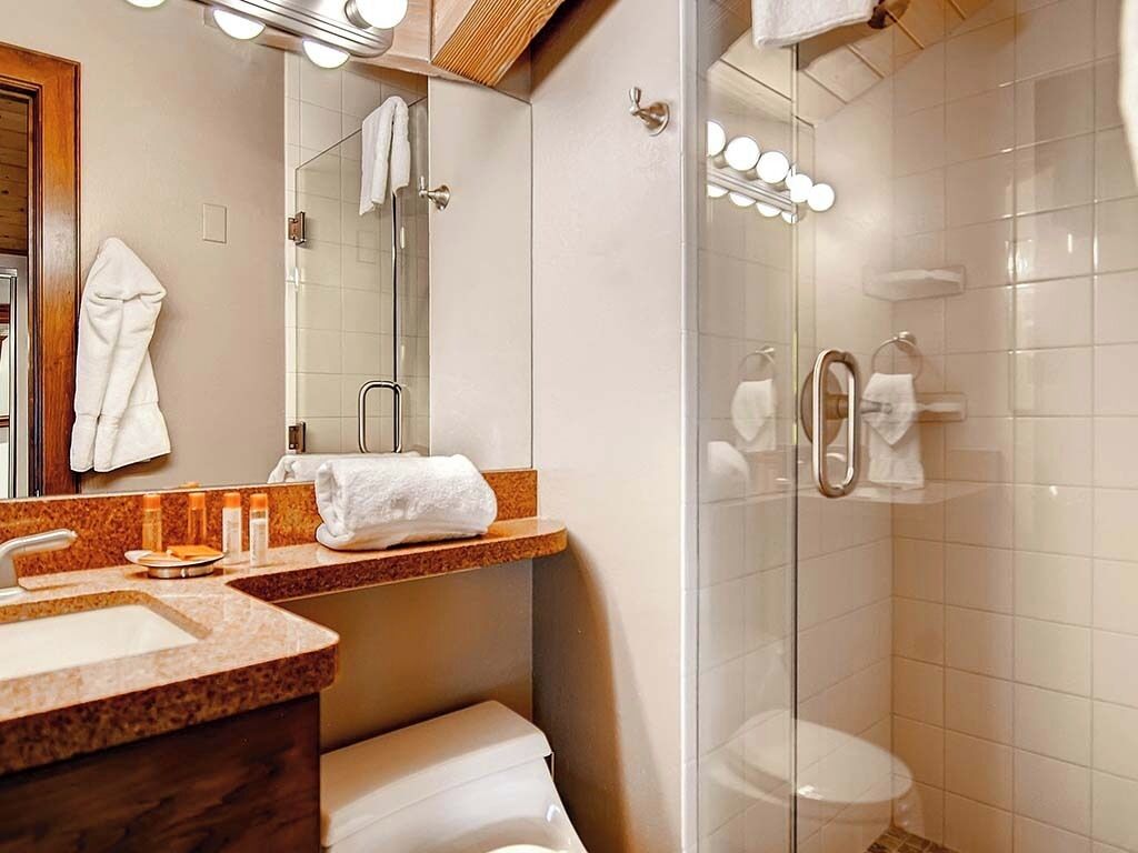 A bathroom with a sink, mirror, towel rack, and a glass-enclosed shower area.