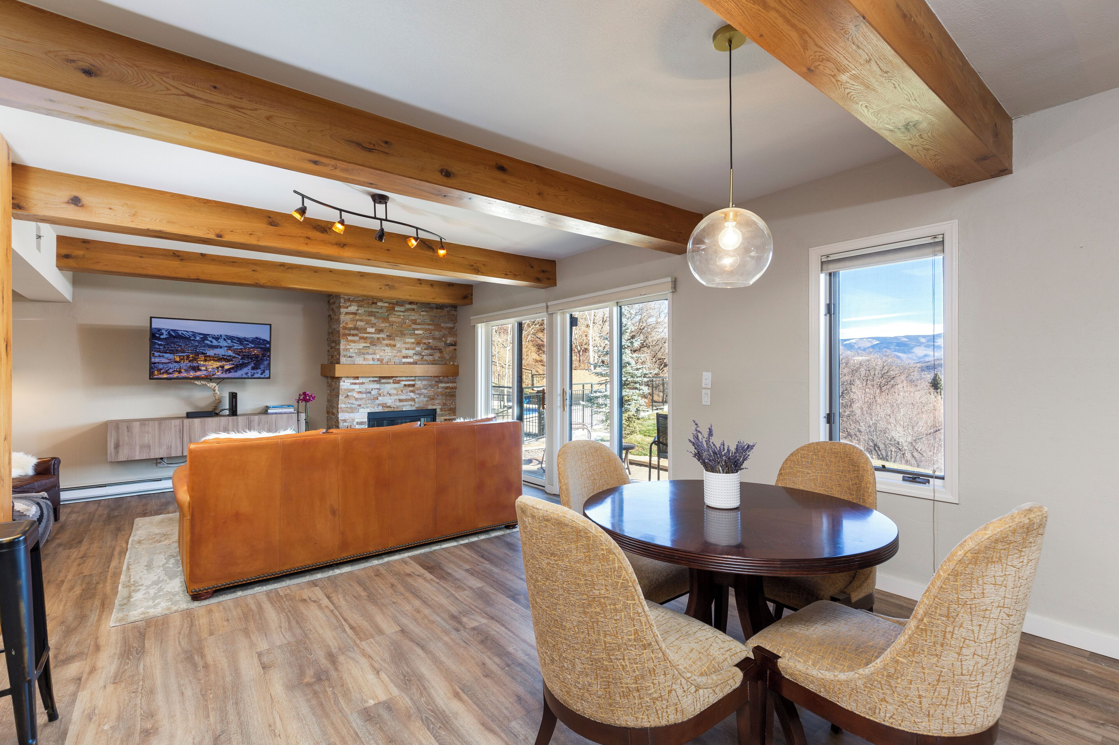 A modern kitchen with a wooden ceiling, a dining area with wicker chairs, and a large window with a view.