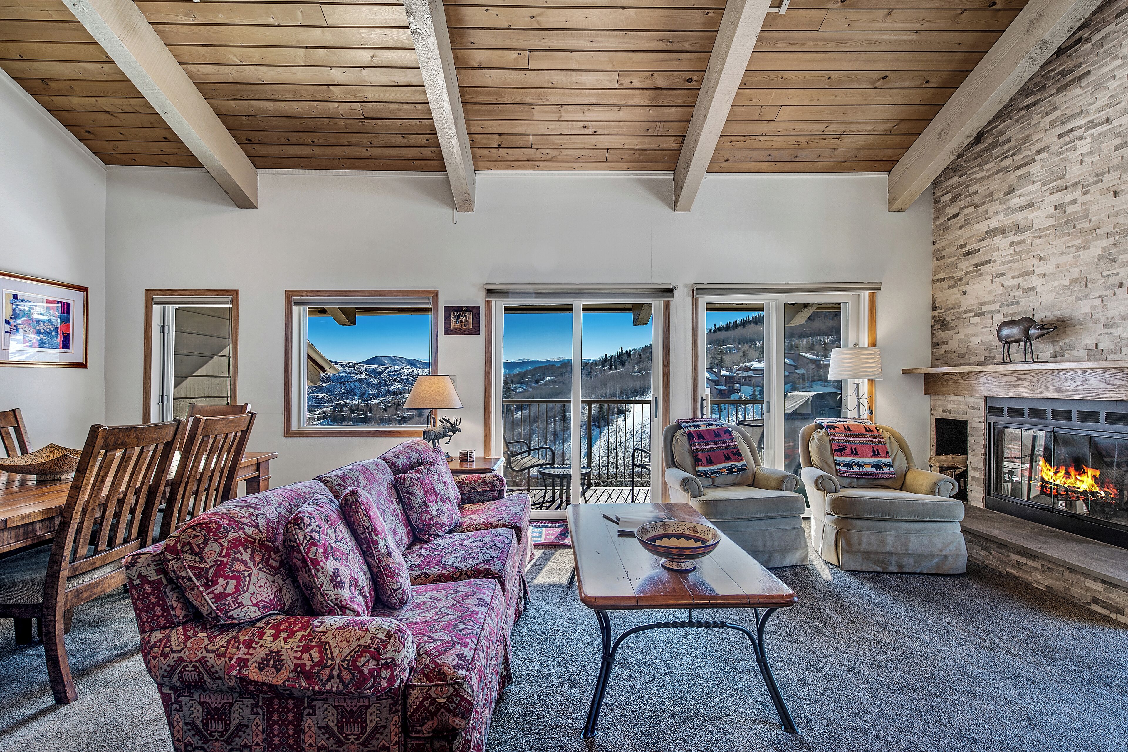 A cozy living room with a fireplace, patterned sofas, and a dining area with wooden furniture.