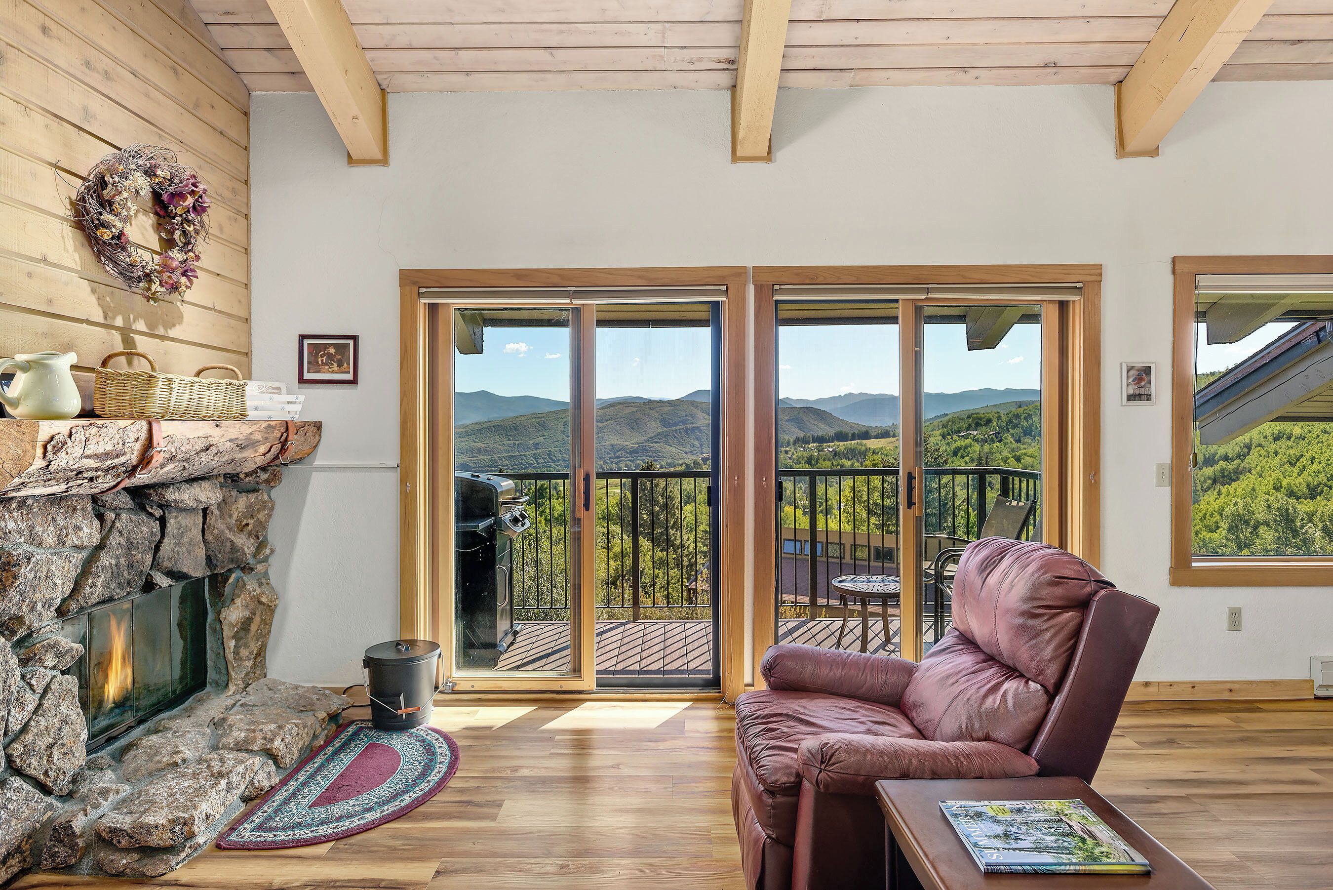 A cozy room with a stone fireplace, a comfortable leather sofa, and a balcony with a scenic mountain view.