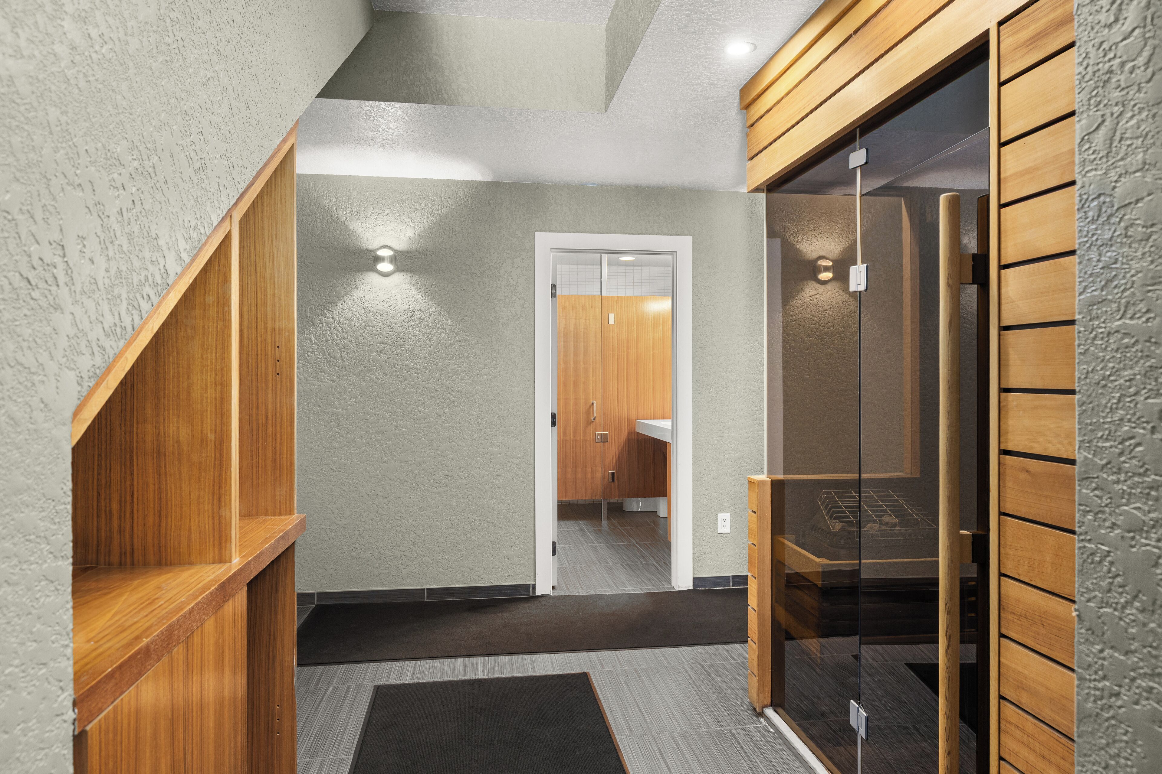 A modern interior with a wooden staircase, a glass door leading to a bathroom, and a dark carpeted floor.
