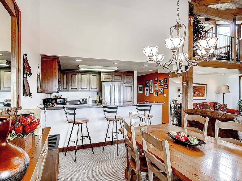 A spacious kitchen with a central island, bar stools, and a chandelier.