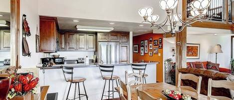 A spacious kitchen with a central island, bar stools, and a chandelier.