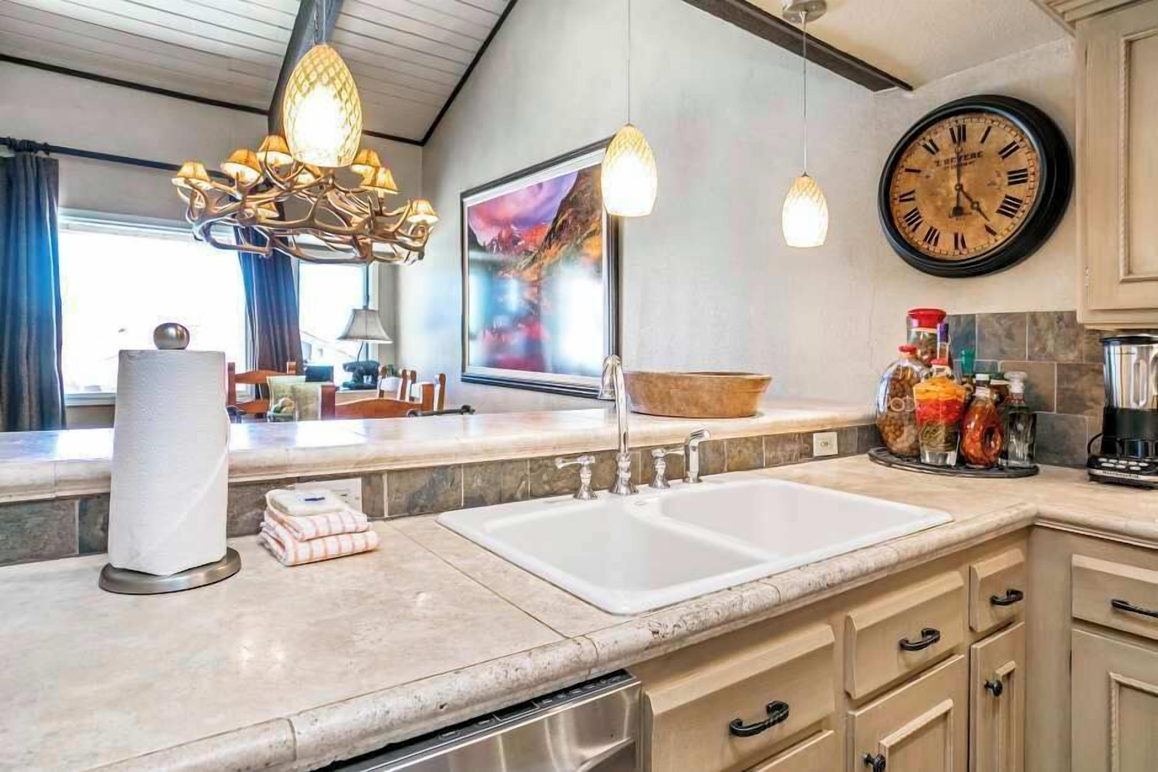 A kitchen with a large sink, a chandelier, a clock, and a painting on the wall.
