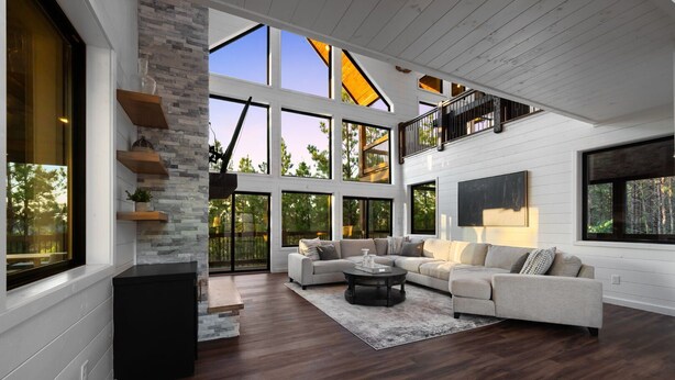 A spacious living room with a large sectional sofa, a coffee table, and a fireplace. There are large windows and a staircase leading to an upper level. - Pool Table, Arcades, Great Views, Pets, Lazy Bear Retreat (Broken Bow)