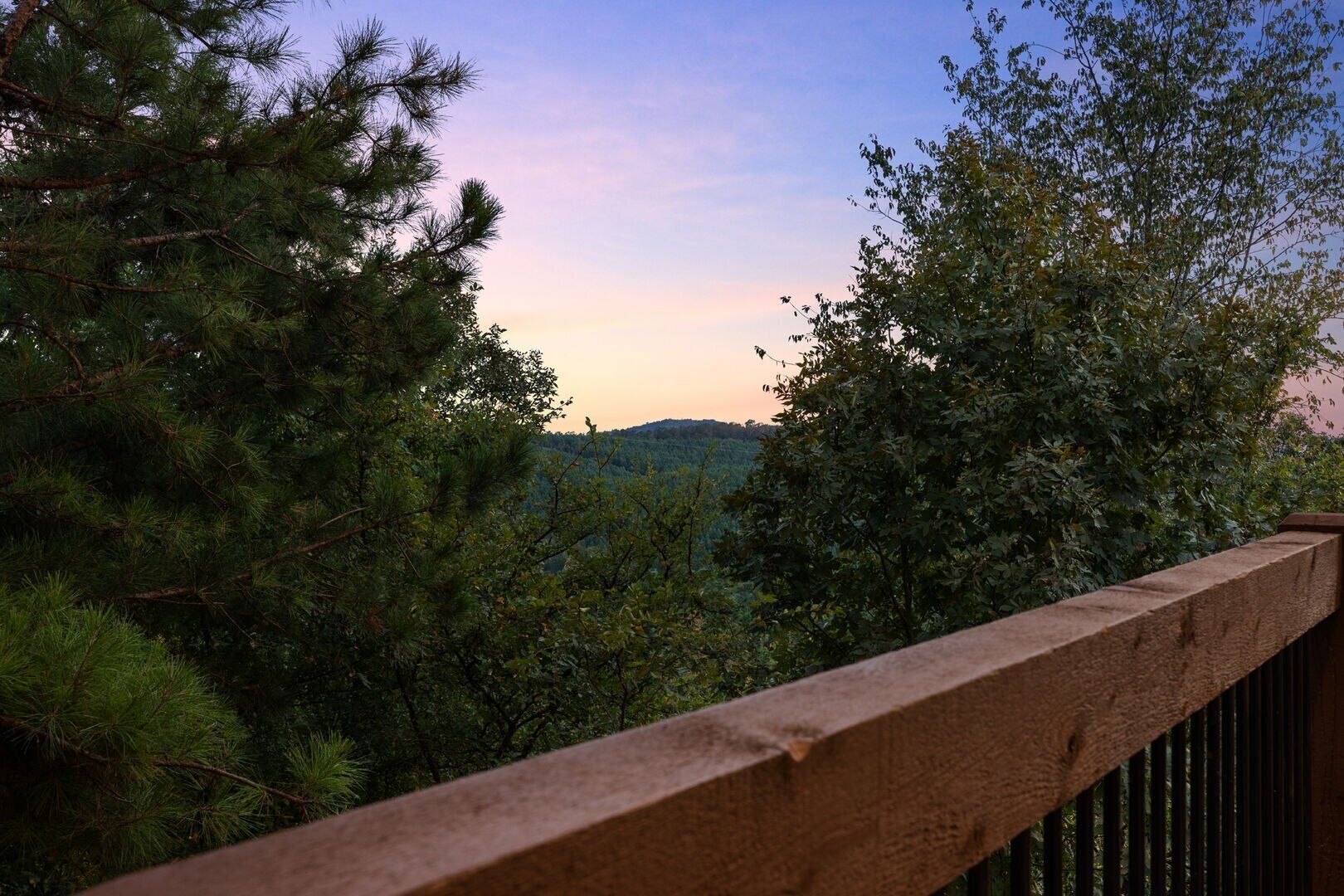 A wooden balcony railing overlooking a forested landscape with a clear sky.
