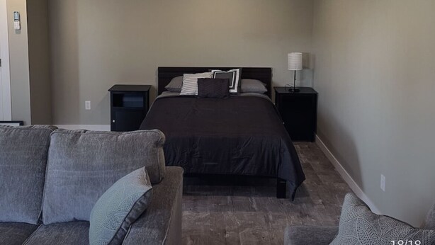A bedroom with a wooden ceiling, a bed with a dark headboard, two bedside tables with lamps, and a gray couch. - WATER FRONT & BACK 4 SEASON GETAWAY AT THE BAY.
Relax with family & friends. (Blenheim)