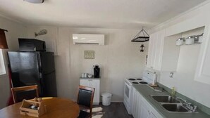 A compact kitchen with a dining table, chairs, a refrigerator, an air conditioner, a stove, and a sink. - WATER FRONT & BACK 4 SEASON GETAWAY AT THE BAY.
Relax with family & friends. (Blenheim)