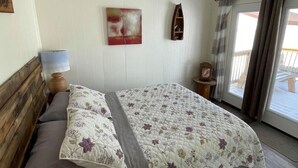 A bedroom with a bed, a nightstand, a lamp, a painting, and a window with curtains. - WATER FRONT & BACK 4 SEASON GETAWAY AT THE BAY.
Relax with family & friends. (Blenheim)