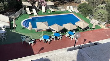 A swimming pool with lounge chairs and tables, surrounded by greenery and trees.