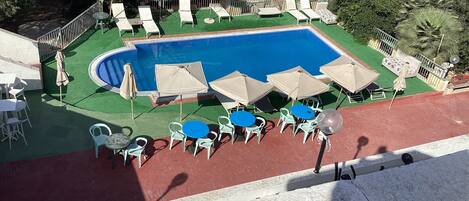 A swimming pool with lounge chairs and tables, surrounded by greenery and trees.