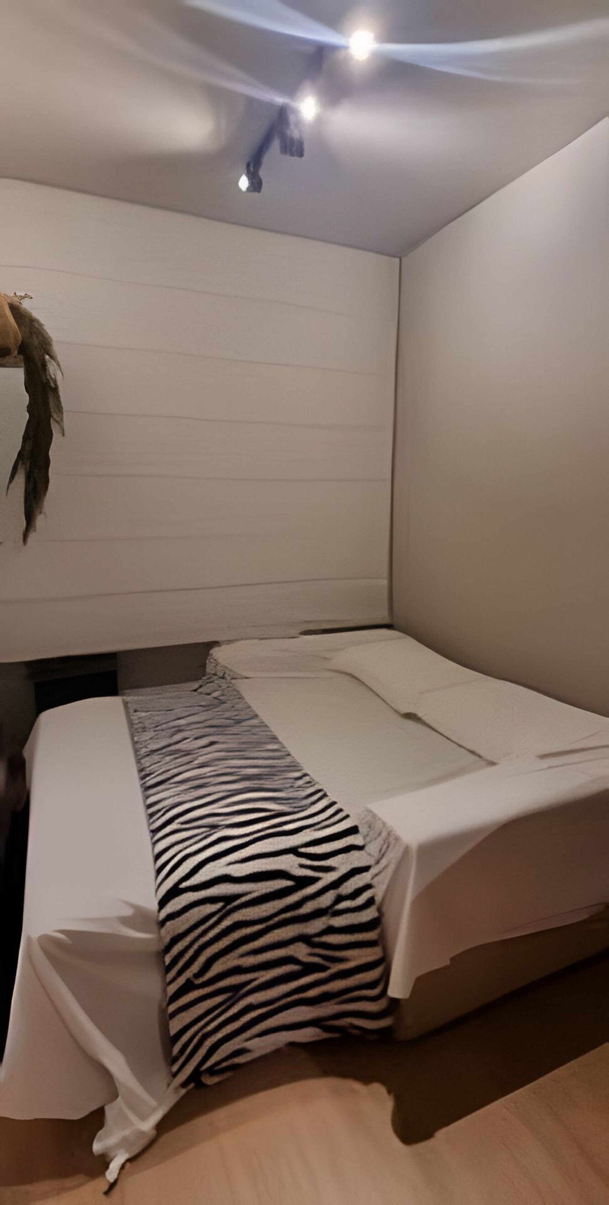 A neatly made bed with a zebra-patterned blanket, a white pillow, and a headboard with a decorative feather.