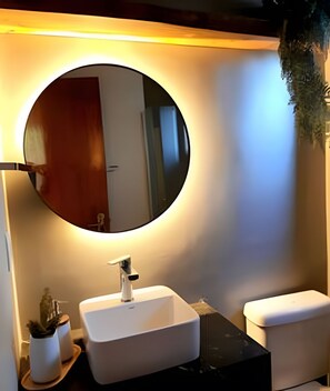 Une salle de bain avec un miroir rond, un lavabo blanc et des toilettes.