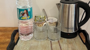 A tray with a water bottle, two glasses, a tea bag, and a stainless steel kettle. - Prithvi Hotel (Rishikesh)