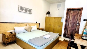 A bedroom with a wooden bed, a nightstand, a desk, and a wardrobe. - Prithvi Hotel (Rishikesh)