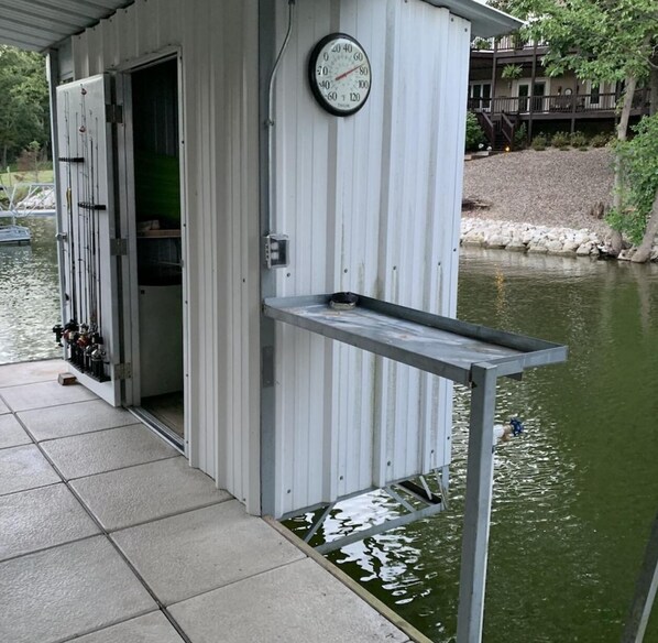 Un edificio metálico con un muelle que se extiende sobre el agua, un reloj en la pared y cañas de pescar afuera.