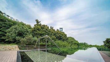 Una piscina de borde infinito de cristal con estructura metálica, rodeada por una terraza de madera y exuberante vegetación.
