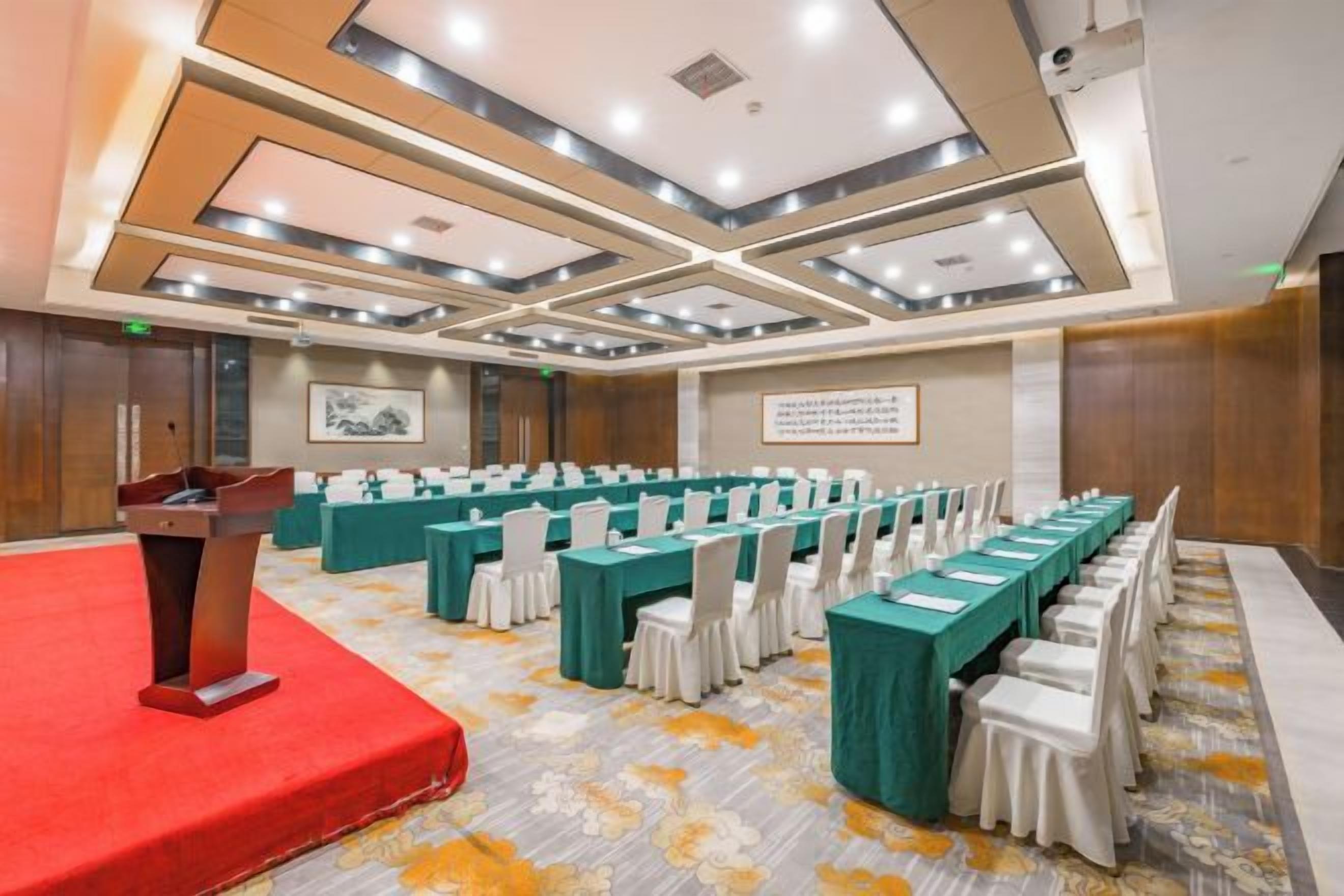 Un salón de conferencias con un atril, filas de mesas y sillas.