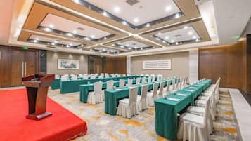 Un salón de conferencias con un atril, filas de mesas y sillas.